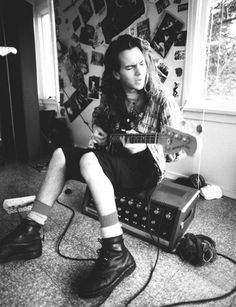 a man sitting on the floor playing an electric guitar with headphones around his neck