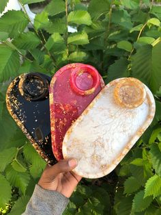 a hand holding three different shaped objects in front of green leaves