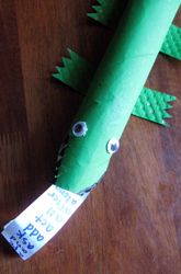 an alligator made out of green paper sitting on top of a wooden table with a price tag attached to it