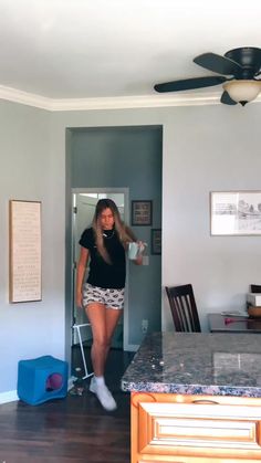 a woman standing in a kitchen next to a table with chairs and a ceiling fan