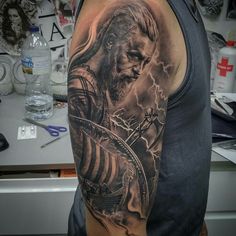 a man's arm with a black and grey tattoo on it, featuring a portrait of jesus