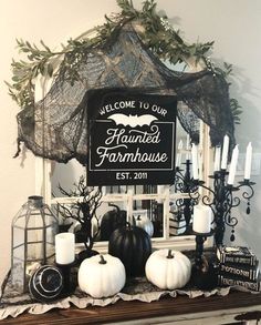 a decorated mantle with candles, pumpkins and other halloween decorations on it in front of a sign that reads welcome to our haunted farmhouse