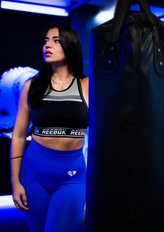 a woman standing next to a punching bag in a blue gym outfit with the words reebuk reese on it