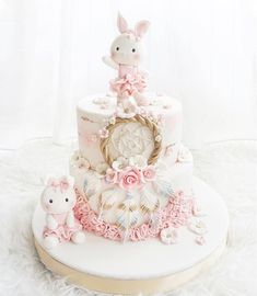 a three tiered cake decorated with pink flowers and bunny figurines