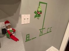 an elf is sitting on the counter in front of a wall with letters and numbers painted on it