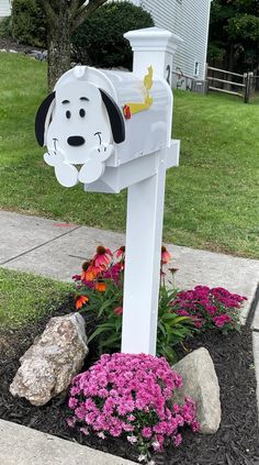 a white mailbox with a dog head on it and flowers in the foreground