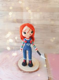 a knitted doll holding a pen on top of a wooden stand with lights in the background