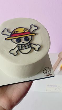 a hand holding a small white cake with a skull and crossbones on it