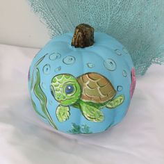 a painted pumpkin with a sea turtle on it's side sitting on a white surface