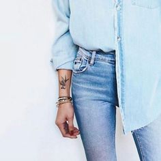 a woman with tattoos on her left arm wearing blue jeans and a button up shirt