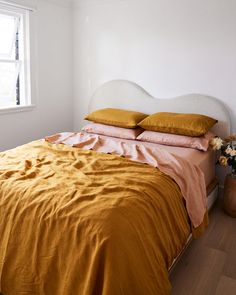 a bed with orange sheets and pillows in a white room next to a potted plant