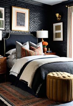 a bedroom with black brick walls, white bedding and an ottoman in the corner