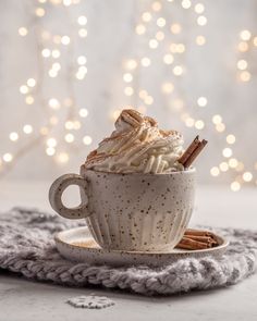 a white cup filled with whipped cream and cinnamon sticks on top of a saucer