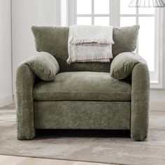 a green chair sitting in front of a window with two pillows on top of it