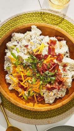 a wooden bowl filled with potato salad next to a glass of wine