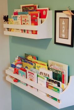 two white shelves with books on them against a green wall in a child's room