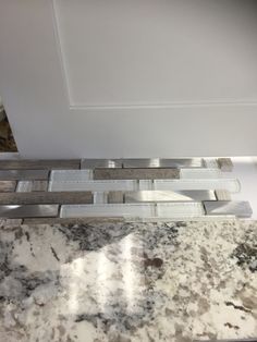 a marble counter top with some silver and white tiles on the bottom, next to a mirror