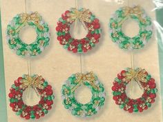 four christmas wreaths hanging from strings on a white sheet with red, green and gold beads