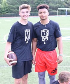 two young men standing next to each other on a field with a football in his hand