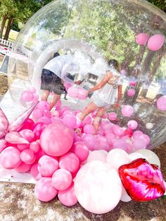 some people are playing in a bubble ball with pink and white balloons on the ground