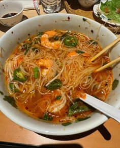 a bowl of noodles with shrimp and spinach on the side next to chopsticks