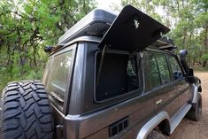 an suv parked on the side of a dirt road with trees in the back ground