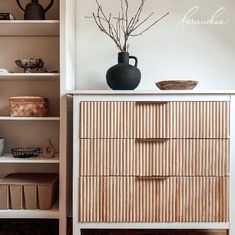 a white dresser with drawers and a black vase on it's top, in front of an open bookcase