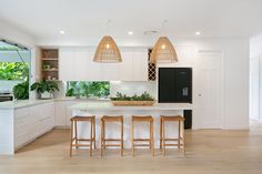 a kitchen with white cabinets and wooden stools in front of an island that has plants on it