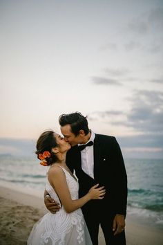 a bride and groom kissing on the beach in front of the ocean at their wedding