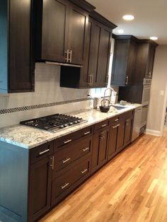 a kitchen with dark wood cabinets and white marble counter tops, along with hardwood flooring