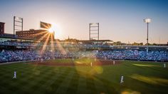 the sun is setting over a baseball field with many people on it and in the stands