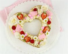 a heart shaped cake decorated with strawberries and flowers on a white plate next to a pink napkin