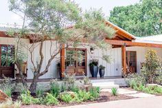 a white house with two large planters on the front porch and trees around it