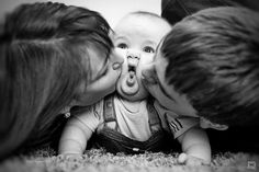 three adults kissing a baby while laying on the floor