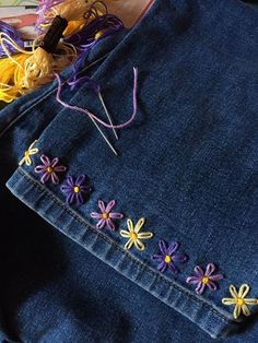 a pair of blue jeans with flowers on the side and yarn in the back pocket