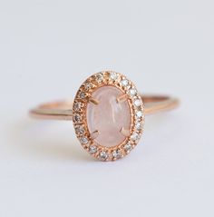 a rose quartz and diamond halo ring on a white surface with the center stone surrounded by small diamonds