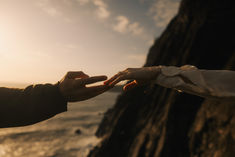 two people reaching out their hands to touch each other's hand near the ocean