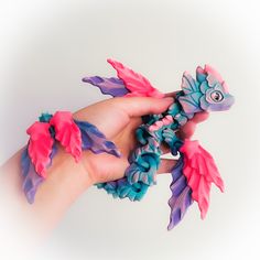 a hand is holding a toy that looks like a fish with pink, blue and purple feathers