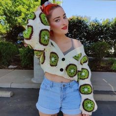 a woman with red hair wearing shorts and a crocheted sweater is posing for the camera