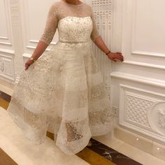 a woman standing in front of a white wall wearing a dress with sheer sleeves and beading