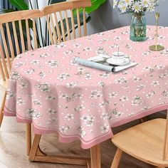 a pink table cloth with white flowers on it in front of a wooden chair and potted plant