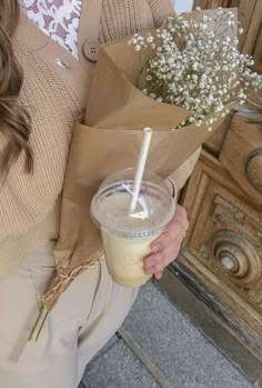 a woman holding a paper cup with a straw and flowers in it