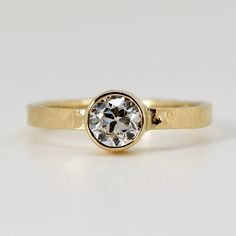 a yellow gold engagement ring with a round cut diamond in the center, on a white background