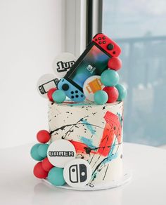 a cake decorated with buttons and video game controllers on it's side, in front of a window