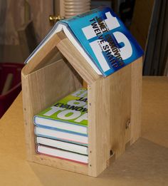 a wooden house shaped like a book holder with books in the front and on top