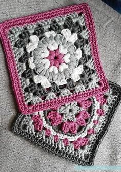 two crocheted squares sitting on top of a bed covered in pink and gray