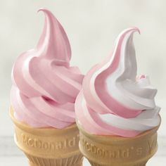 two ice cream cones with pink and white frosting on top, sitting next to each other