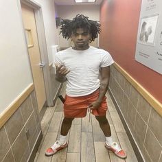 a young man with dreadlocks standing in a hallway wearing orange shorts and white t - shirt