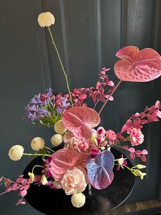 a black vase with pink and purple flowers in it on a table next to a door