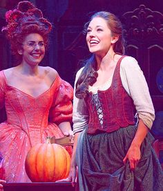 two women dressed in costumes smile as they stand next to each other with pumpkins